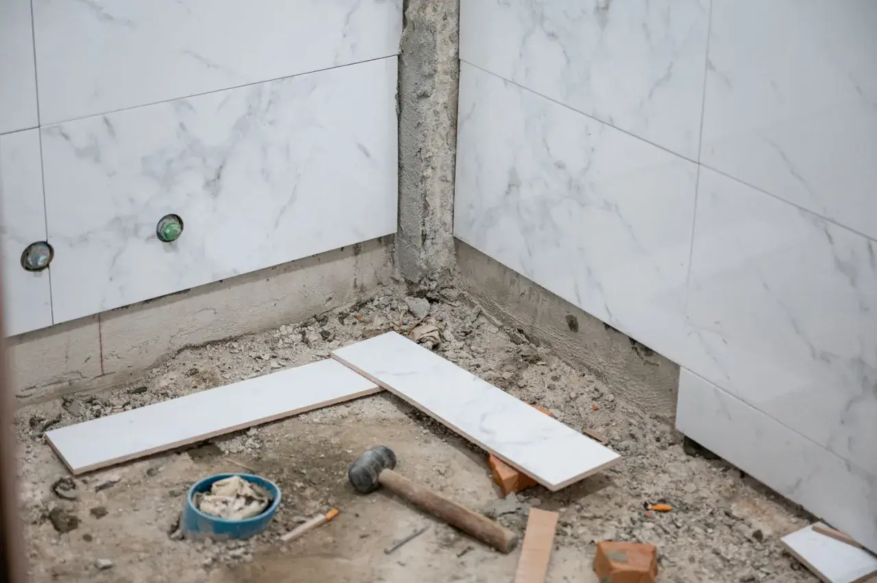 Travaux de salle de bain : pose de carreaux sur du carrelage existant. Marteau, briques et carreaux blancs sont prêts pour le chantier.