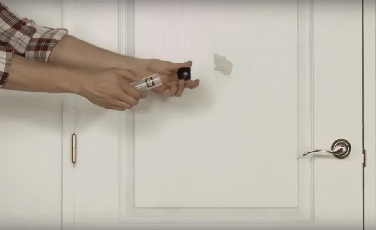 Un homme montre comment réparer un trou dans une porte avec un kit de réparation.