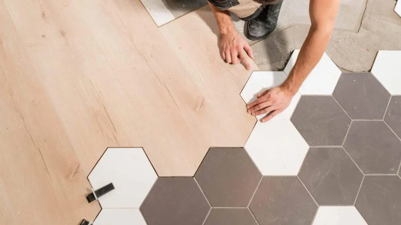 Pose d'un parquet en bois clair à la jonction avec un carrelage hexagonal gris et blanc.