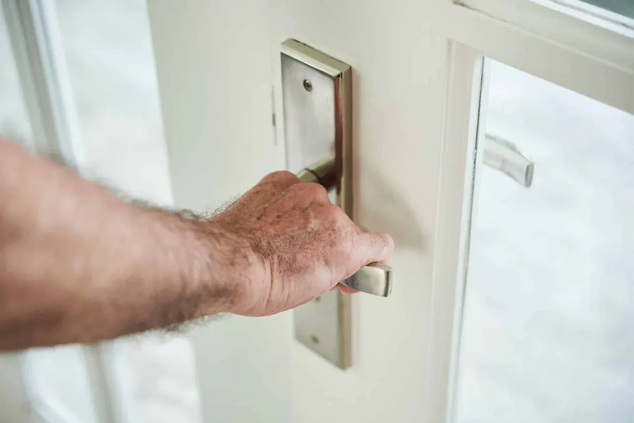 Main d'homme saisissant la poignée d'une porte blanche, prête à en modifier le sens d'ouverture.