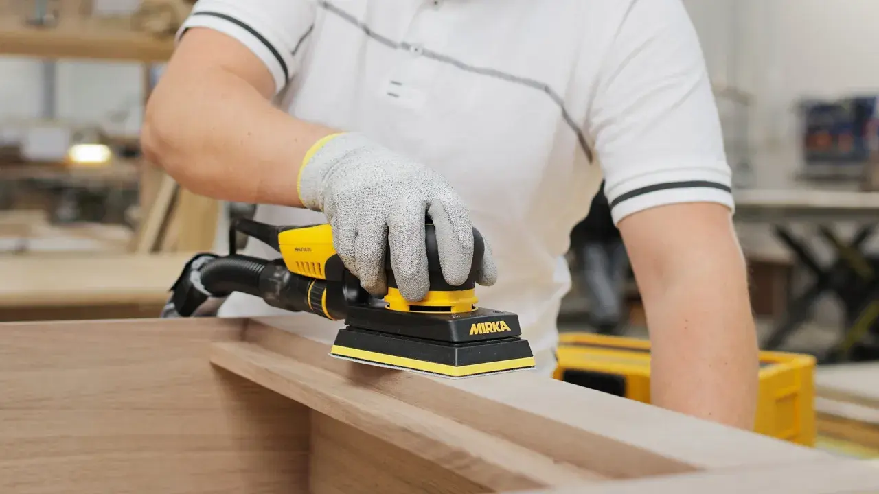 Un artisan utilise une ponceuse pour porte en bois, préparant une surface lisse pour un projet de menuiserie.