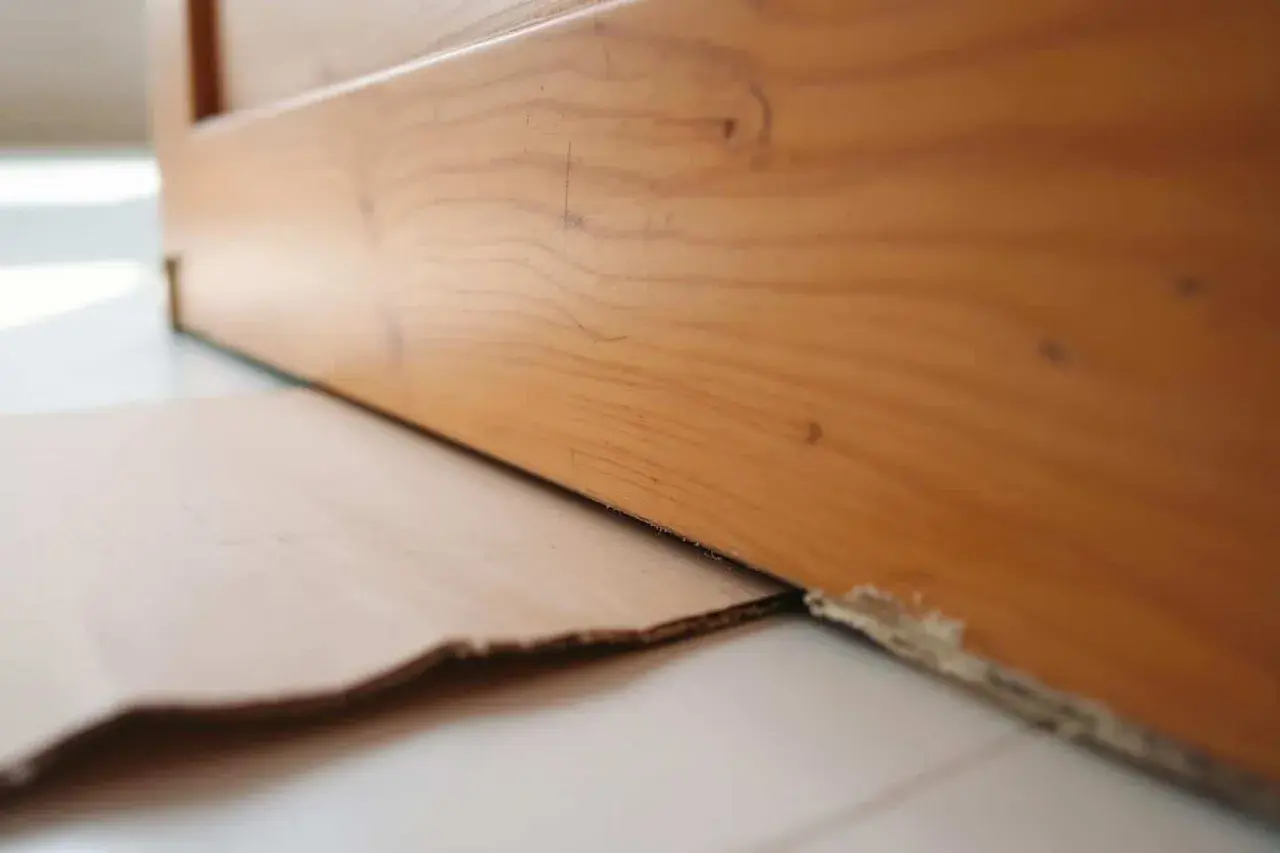 Le bas d'une porte en bois est légèrement surélevé, révélant un espace où du carton est glissé pour le détalonnage.