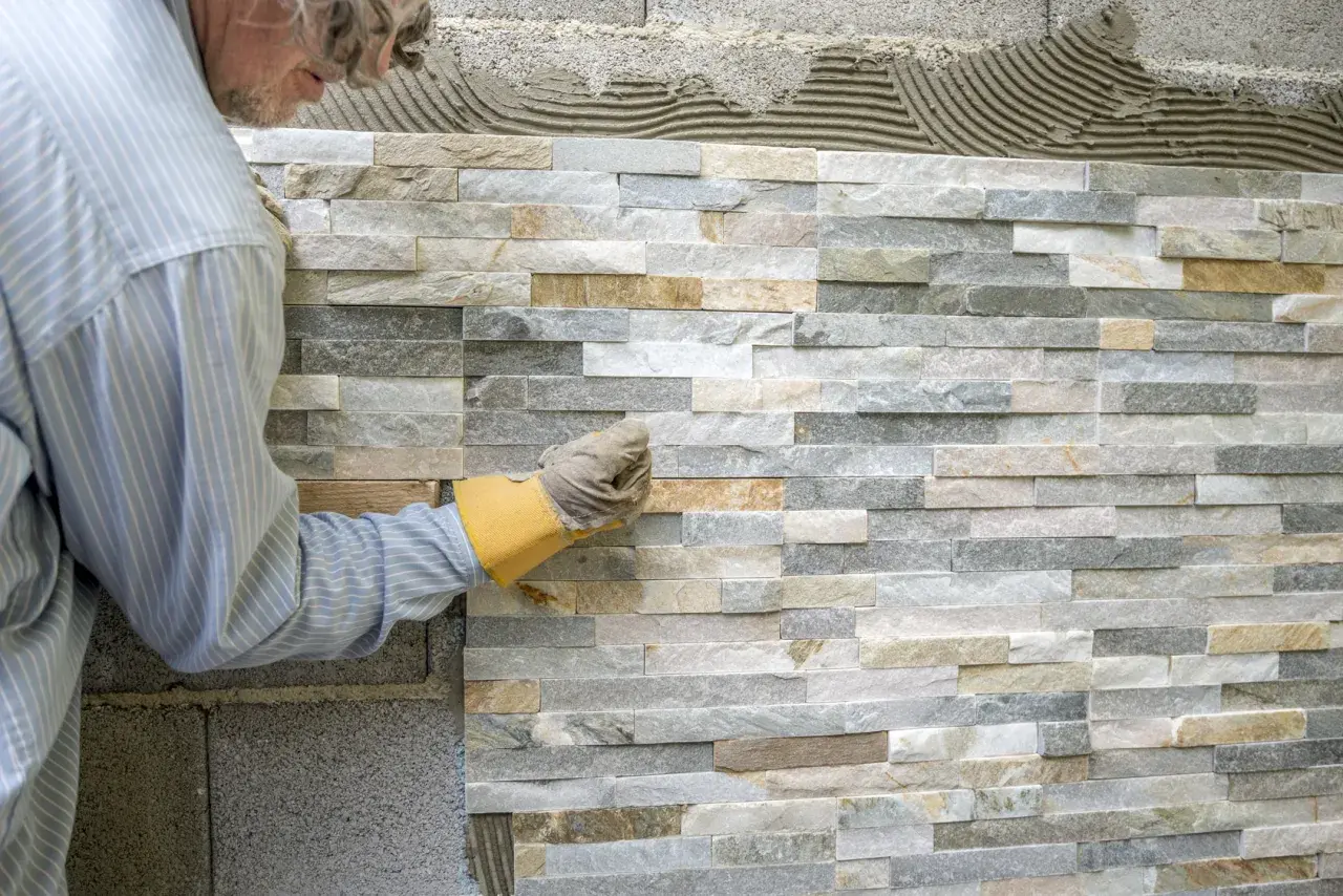 Pose de pierre de parement intérieur, un artisan ajuste une pierre sur un mur en cours de finition.