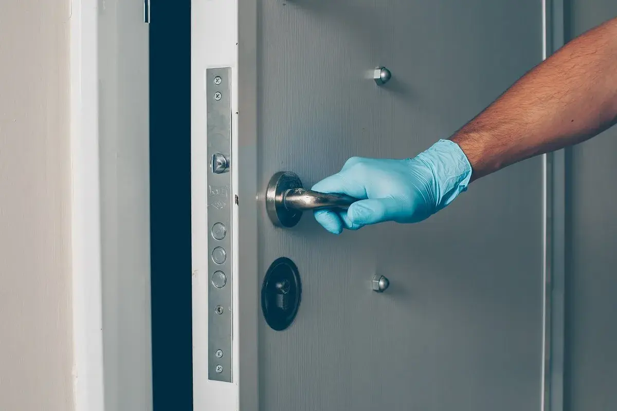 Main tenant, ganté, ouvre une porte voilée.