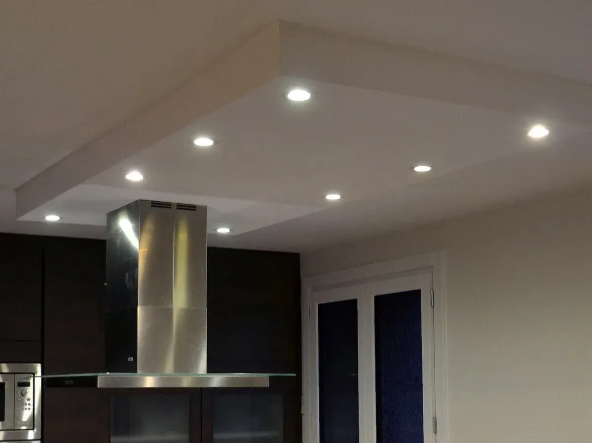 Un caisson plafond avec spots éclaire une cuisine moderne. La hotte en inox et les meubles sombres créent un contraste élégant.