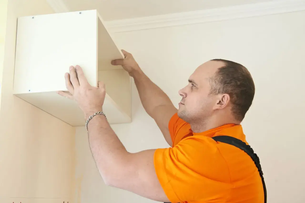 Un homme en t-shirt orange est en train de fixer un caisson blanc au mur.