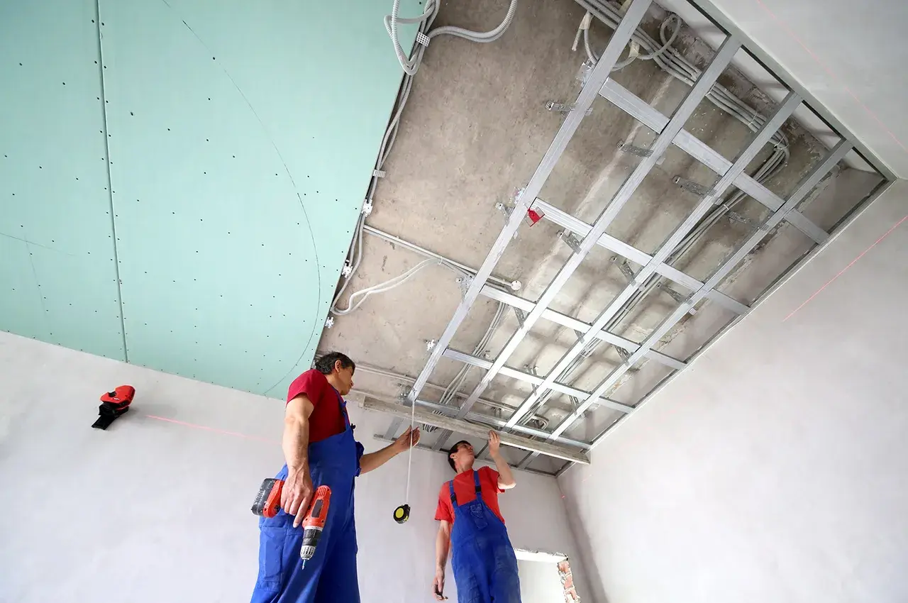 Deux ouvriers installent une structure métallique pour un schema montage placo plafond. Des fils électriques sont déjà en place.