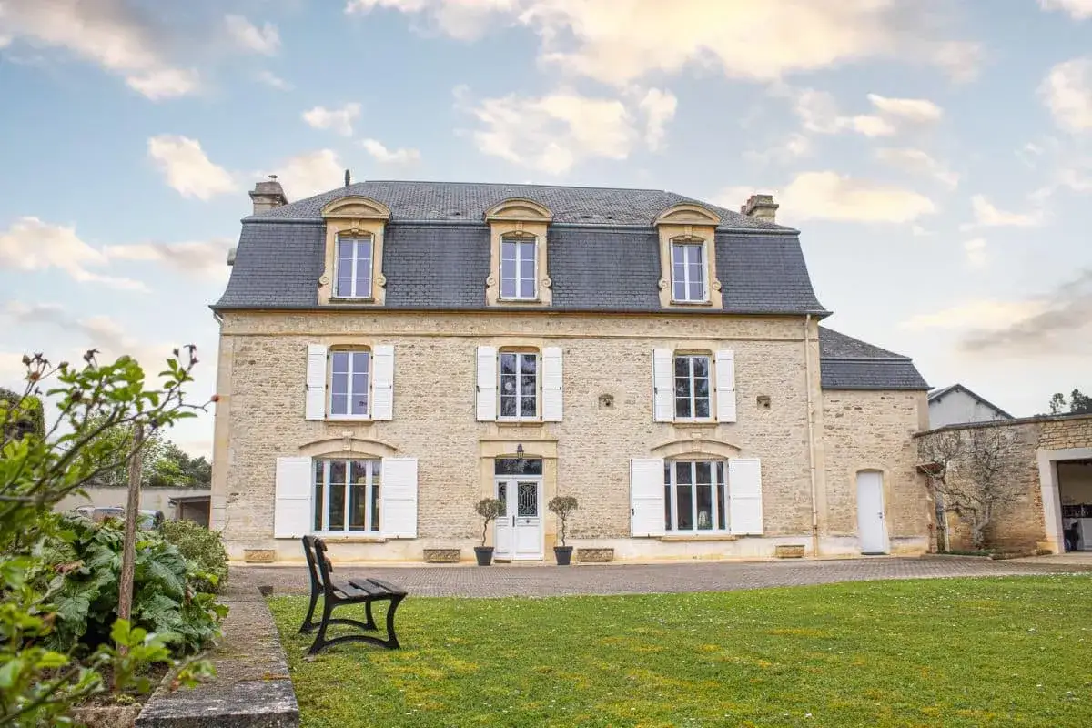 Belle maison en pierre avec une installation de volets battants blancs, un jardin verdoyant et un ciel nuageux.