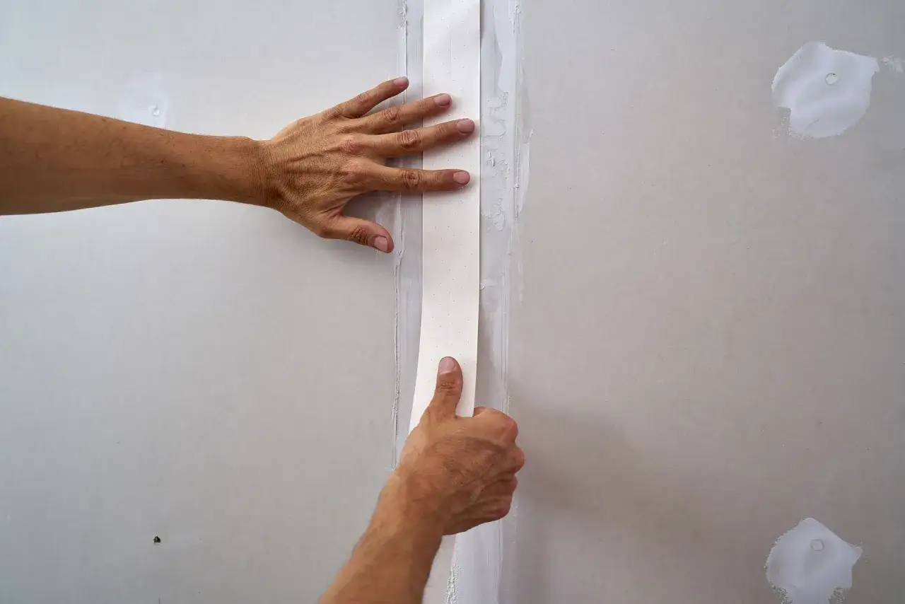Mains appliquant une bande de papier sur un joint de placo. La question 