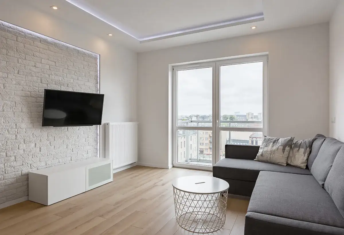 Salon moderne avec TV murale. La norme hauteur TV par rapport au sol est respect&eacute;e pour un confort visuel optimal. Canap&eacute; gris, table basse et parquet clair.