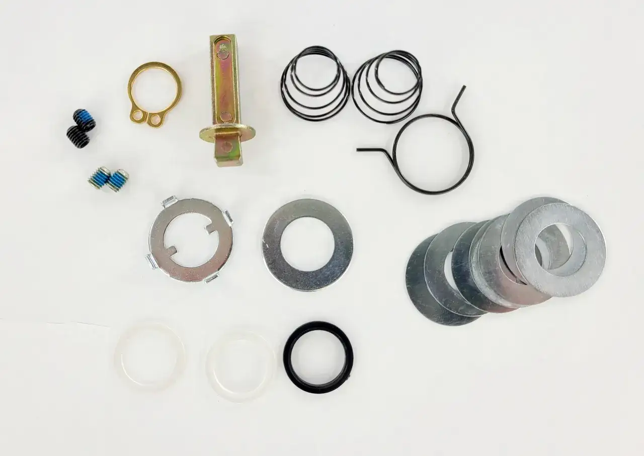 Kit de pièces pour changer poignée de porte : vis, ressorts, rondelles, axe et anneau de fixation.