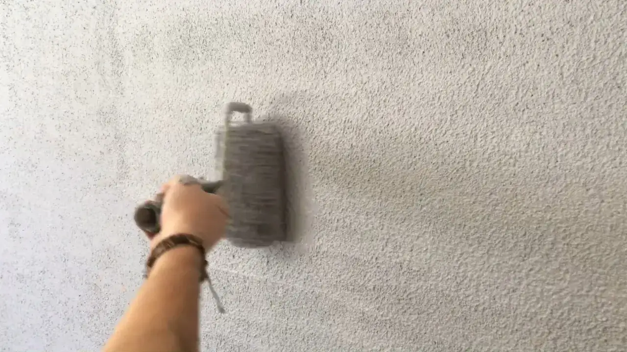 Main d'une personne appliquant un cr&eacute;pi au rouleau sur un mur textur&eacute;.