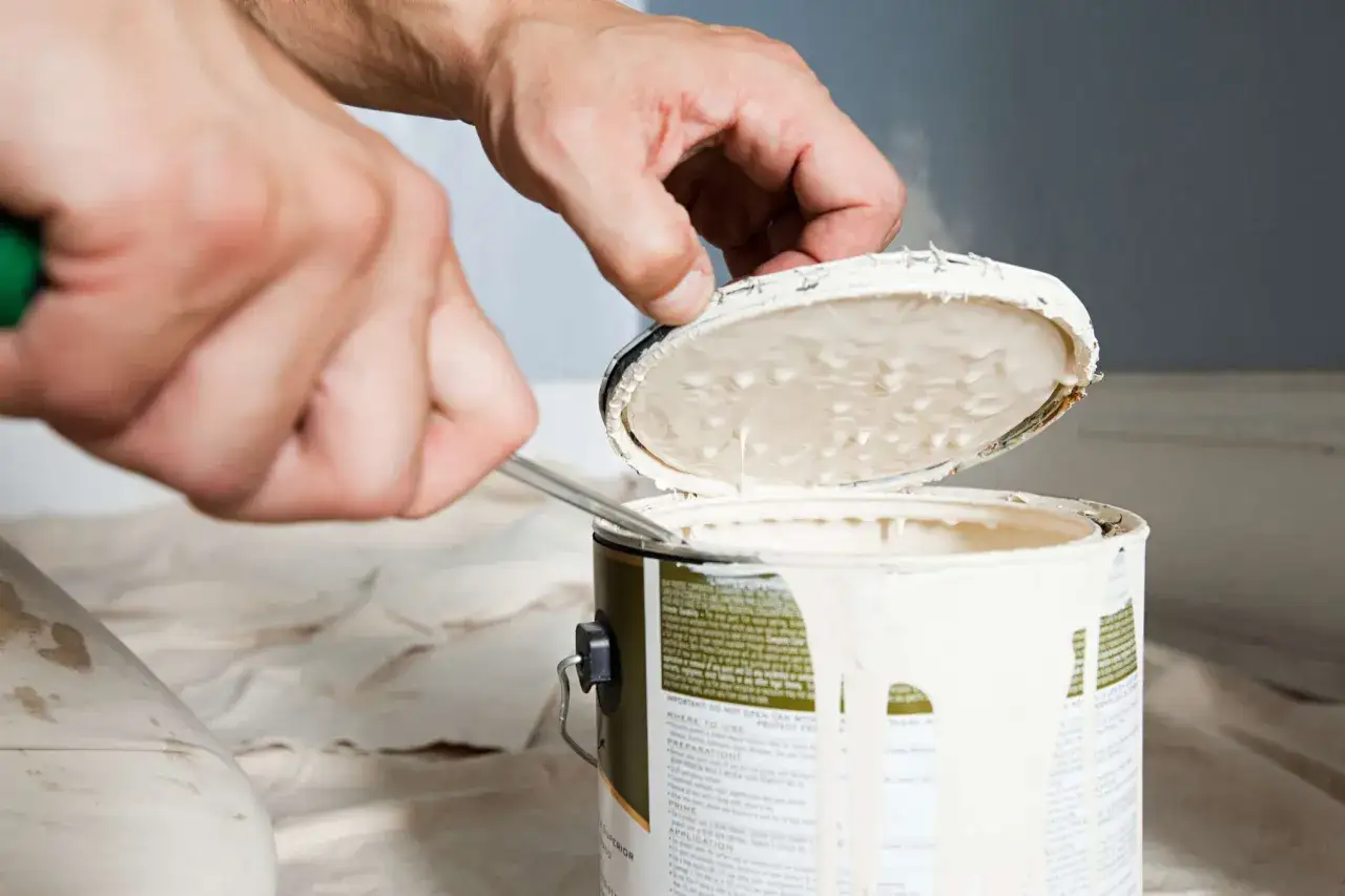 Main tenant, avec un tournevis, ouvre un pot de peinture blanc. La peinture coule sur le bord.