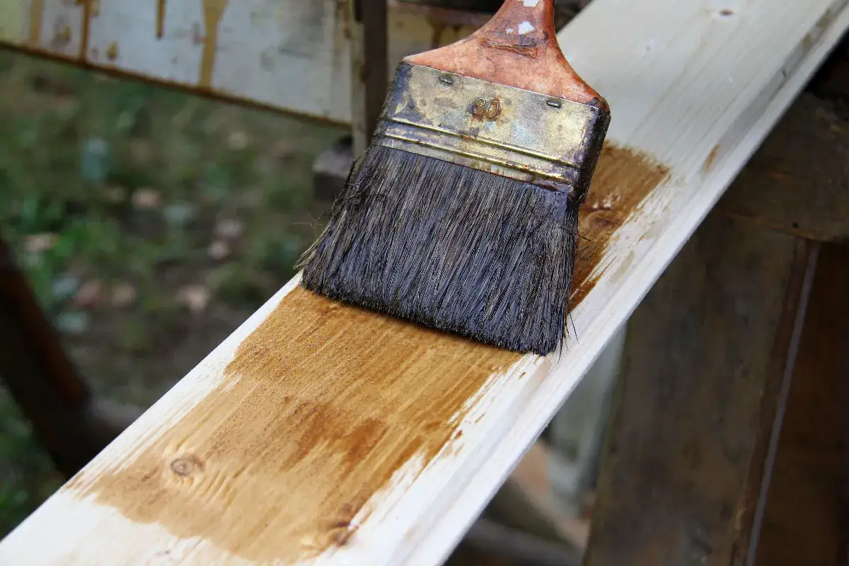 Application d'une lasure sur une planche de bois clair, peut-être pour une future fenêtre en bois.