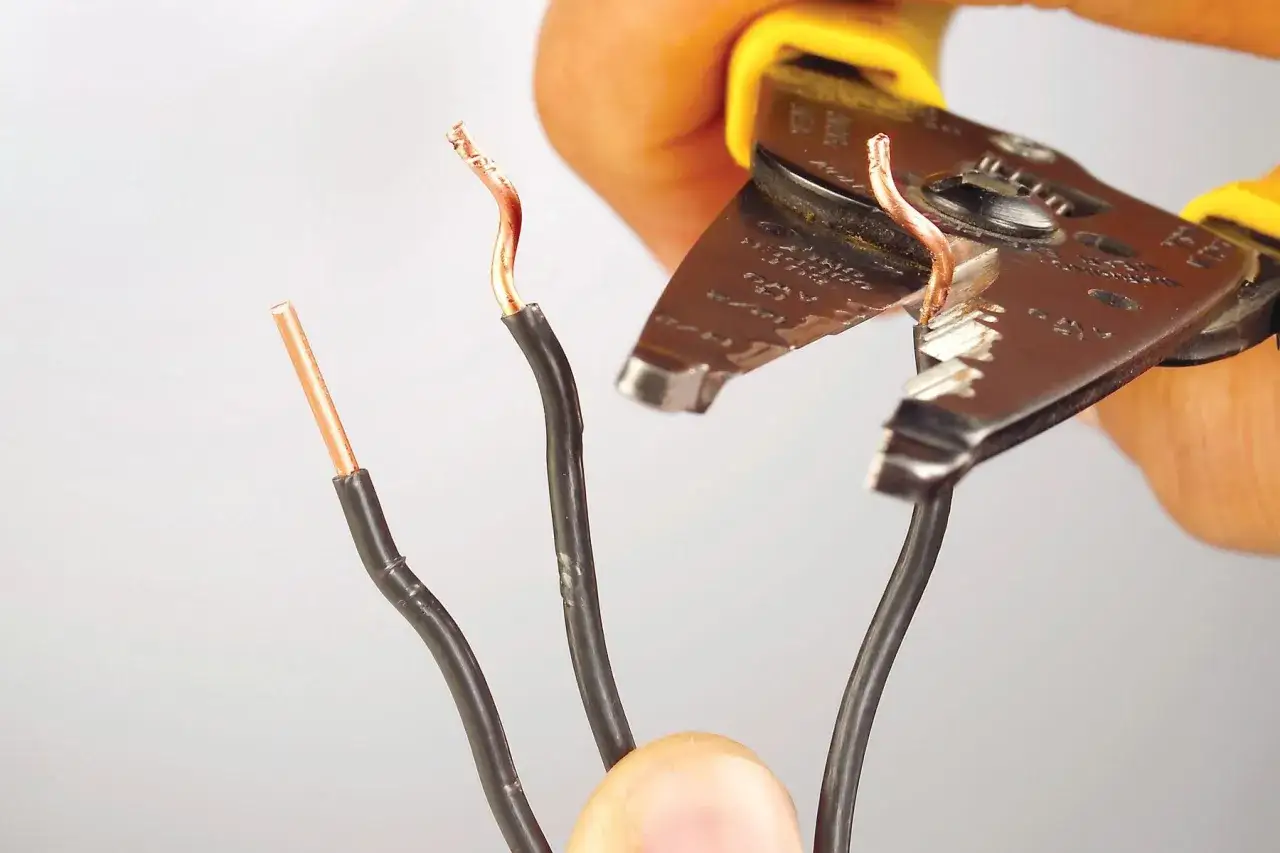 Main tenant utilise une pince pour raccorder 2 fils électriques sans domino. Les fils de cuivre dénudés sont prêts à être connectés.