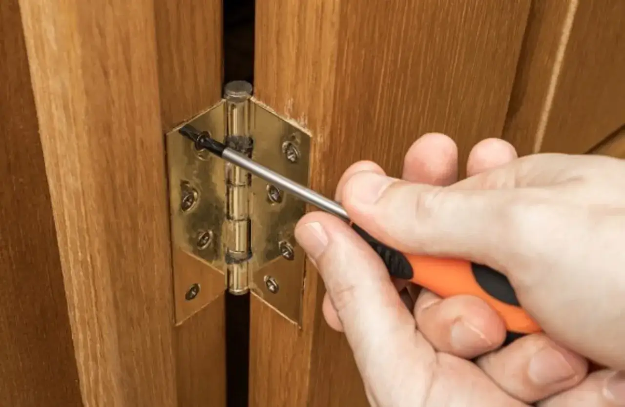 Main tenant une visseuse, une personne ajuste une charnière plate sur une porte en bois.