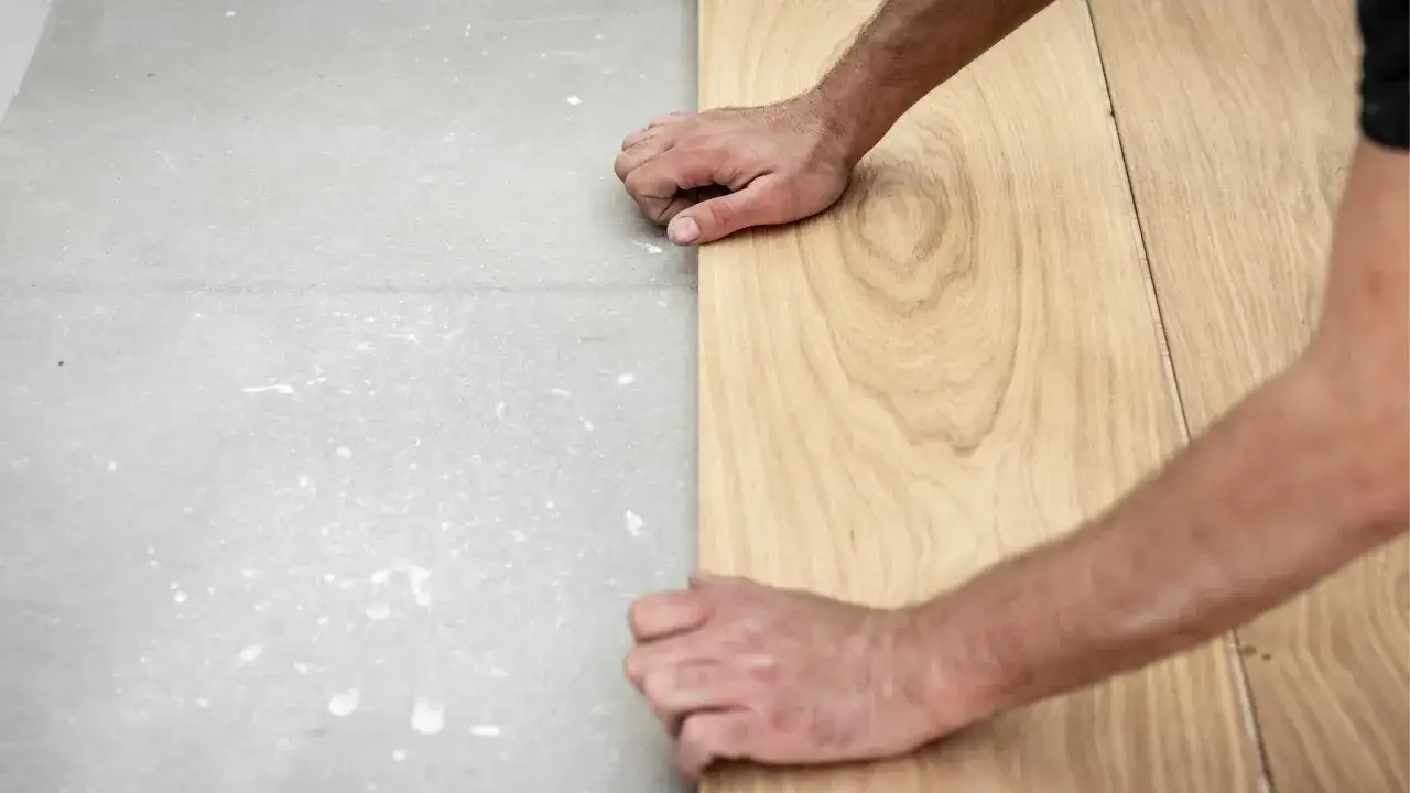 Pose de carrelage imitation parquet : mains ajustant une lame de bois sur un sol brut.