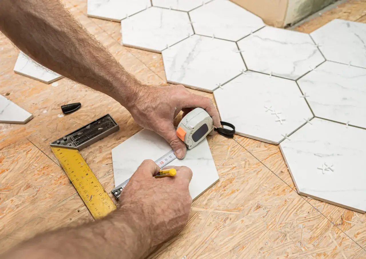 Pose de carreaux hexagonaux sur plancher OSB. Un carreleur mesure une pièce avant la pose.