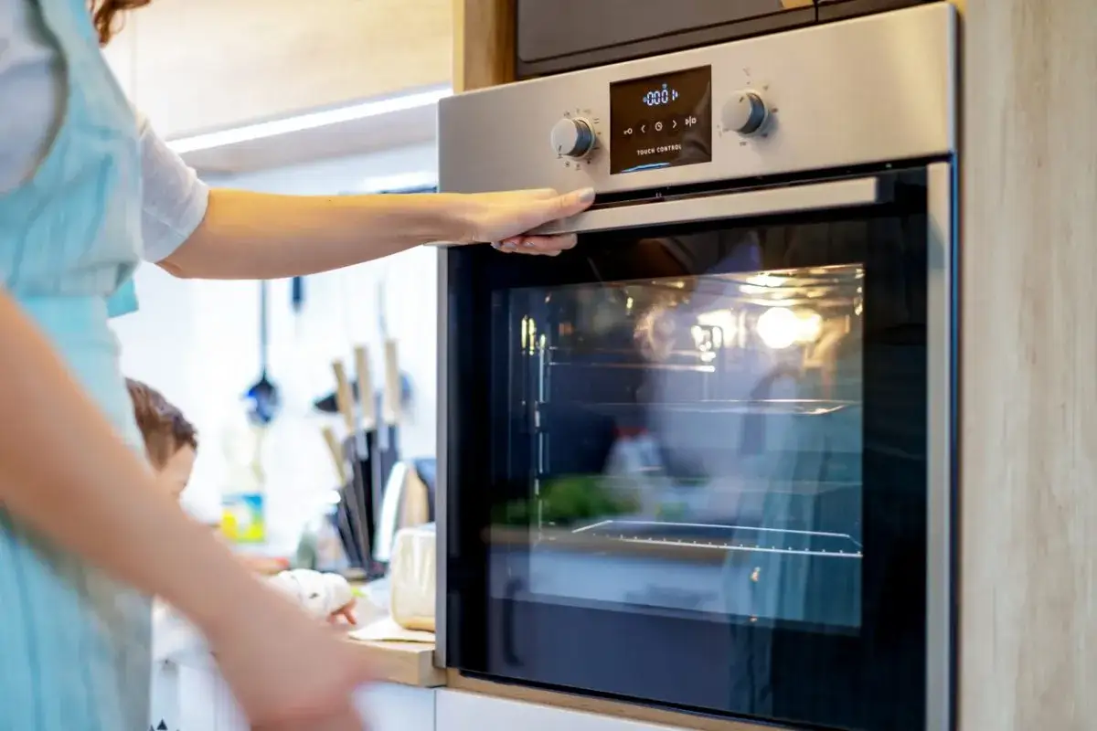 Une main ouvre la porte vitr&eacute;e d'un four moderne. La prise m&acirc;le pour four est discr&egrave;tement int&eacute;gr&eacute;e.