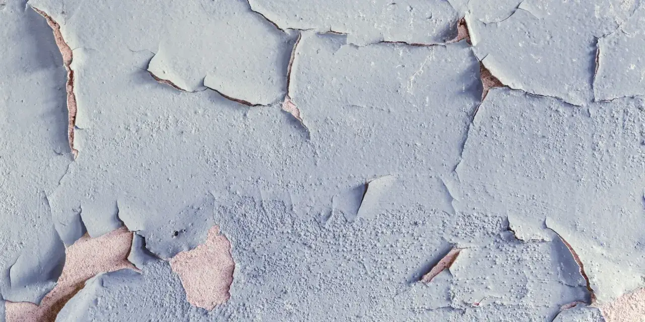 Texture d'un mur ancien avec de la peinture &eacute;caill&eacute;e r&eacute;v&eacute;lant la couche inf&eacute;rieure ros&eacute;e. Les fissures cr&eacute;ent un motif abstrait.