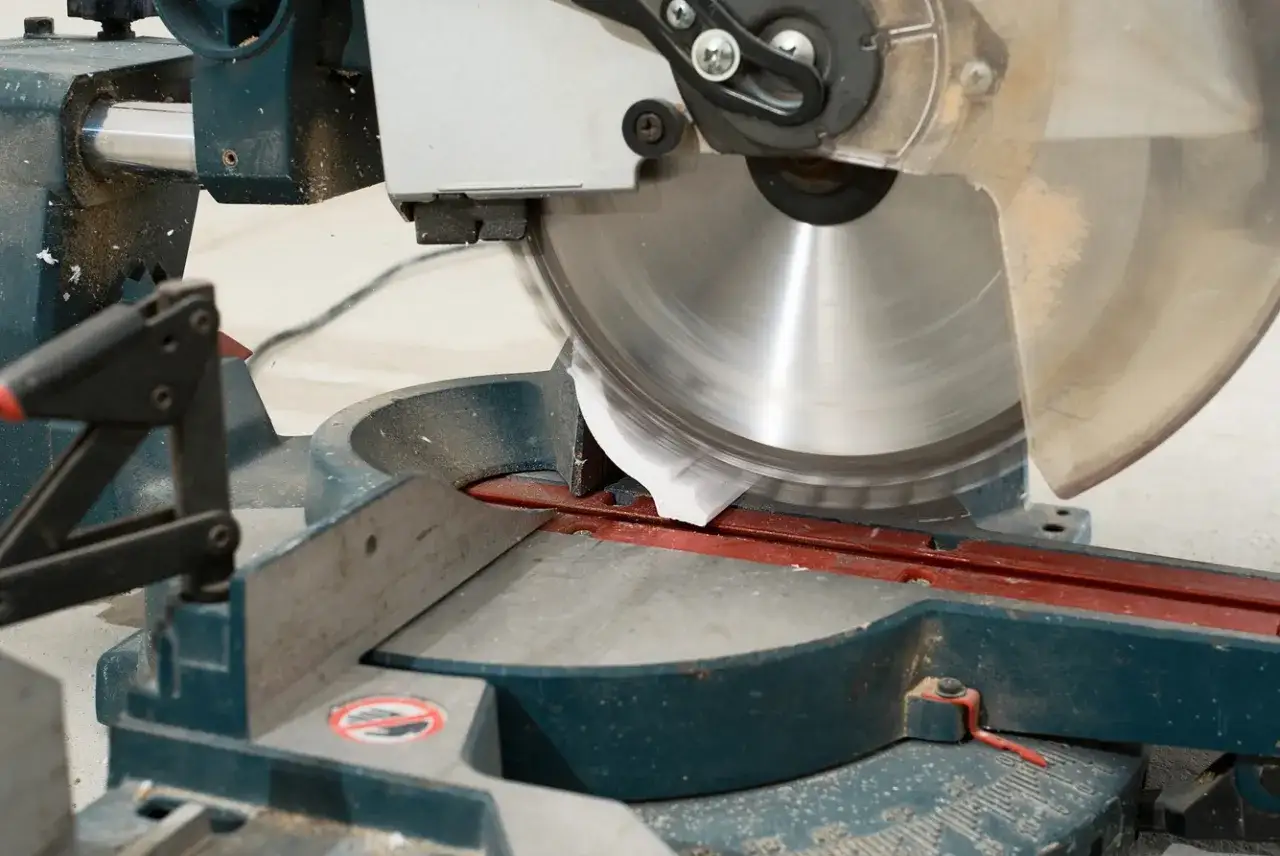 Une scie circulaire de menuiserie coupe une moulure. La lame tourne rapidement, prête à découper avec précision.