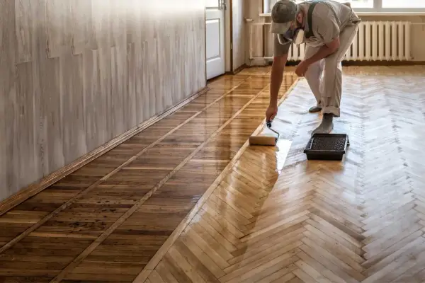 Pose de carrelage imitation parquet : un professionnel applique une couche protectrice sur un sol en chevrons.