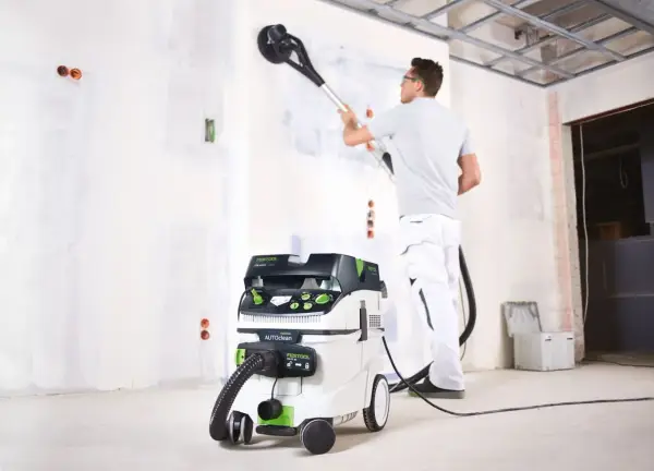 Un ouvrier utilise un aspirateur pour girafe afin de poncer un mur.